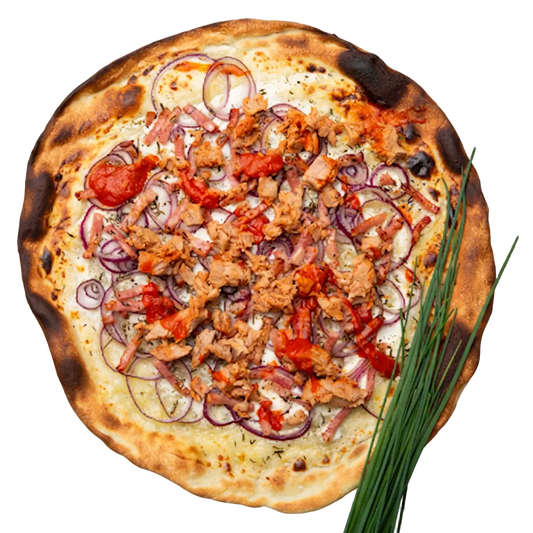 A round flatbread pizza topped with sliced red onion, chunks of cooked meat, diced red tomatoes, and herbs, shown on a transparent checkerboard background with green chives placed along the lower right side.
